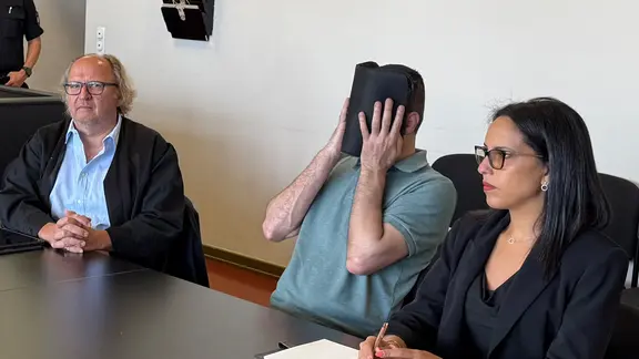 Eine Angeklagter sitzt im Gerichtssaal in Hamburg und verdeckt sein Gesicht.
