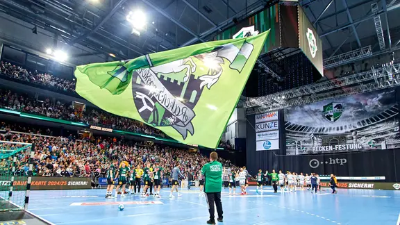 Ein Mann schwenkt vor Fans in der ZAG Arena die Flagge des Handball-Bundesligisten Hannover-Burgdorf.