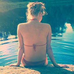 Eine junge Frau in Bikini sitzt an einem Gewässer