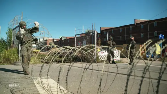 Ein Bundeswehrsoldat spannt einen Stacheldraht vor einer Einfahrt.