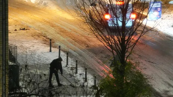 Hamburg: Ein Mann räumt am frühen Morgen den Schnee mit einem Besen von einem Gehweg.