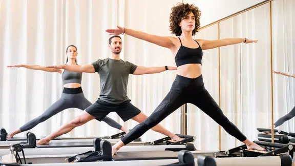 Drei Menschen trainieren Pilates am Reformer