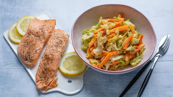 Wokgemüse, daneben auf einem Brett zwei gegrillte Lachsfilets.