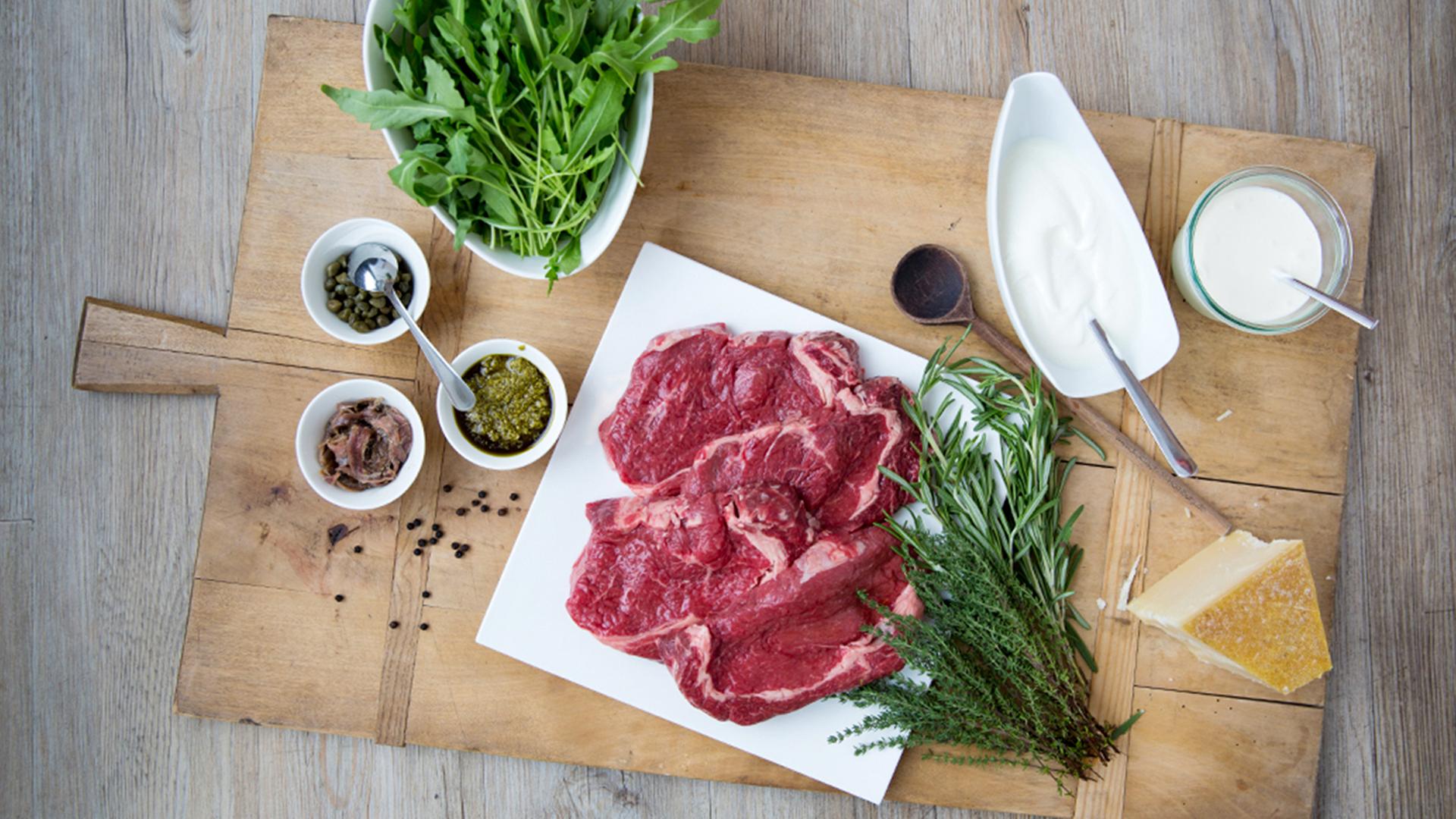 Rindfleisch, eine Schüssel mit Joghurt, eine Schüssel mit Creme Fraiche, Rucola,Kapern, Sardellen, Parmesan, ein Holzlöffel und Pfefferkörner liegen auf einem Brett. | NDR, Claudia Timmann