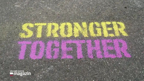 Bunte Kreidebotschaft "STRONGER TOGETHER" auf Asphalt geschrieben.