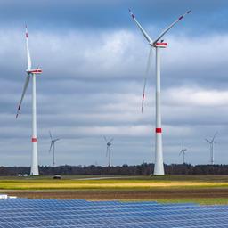 Photovoltaikanlagen stehen auf einem Feld vor mehreren Windrädern.
