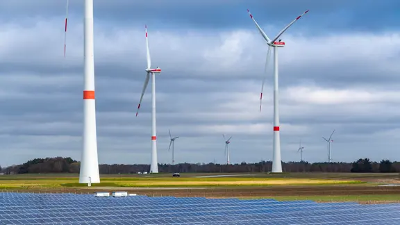 Photovoltaikanlagen stehen auf einem Feld vor mehreren Windrädern.