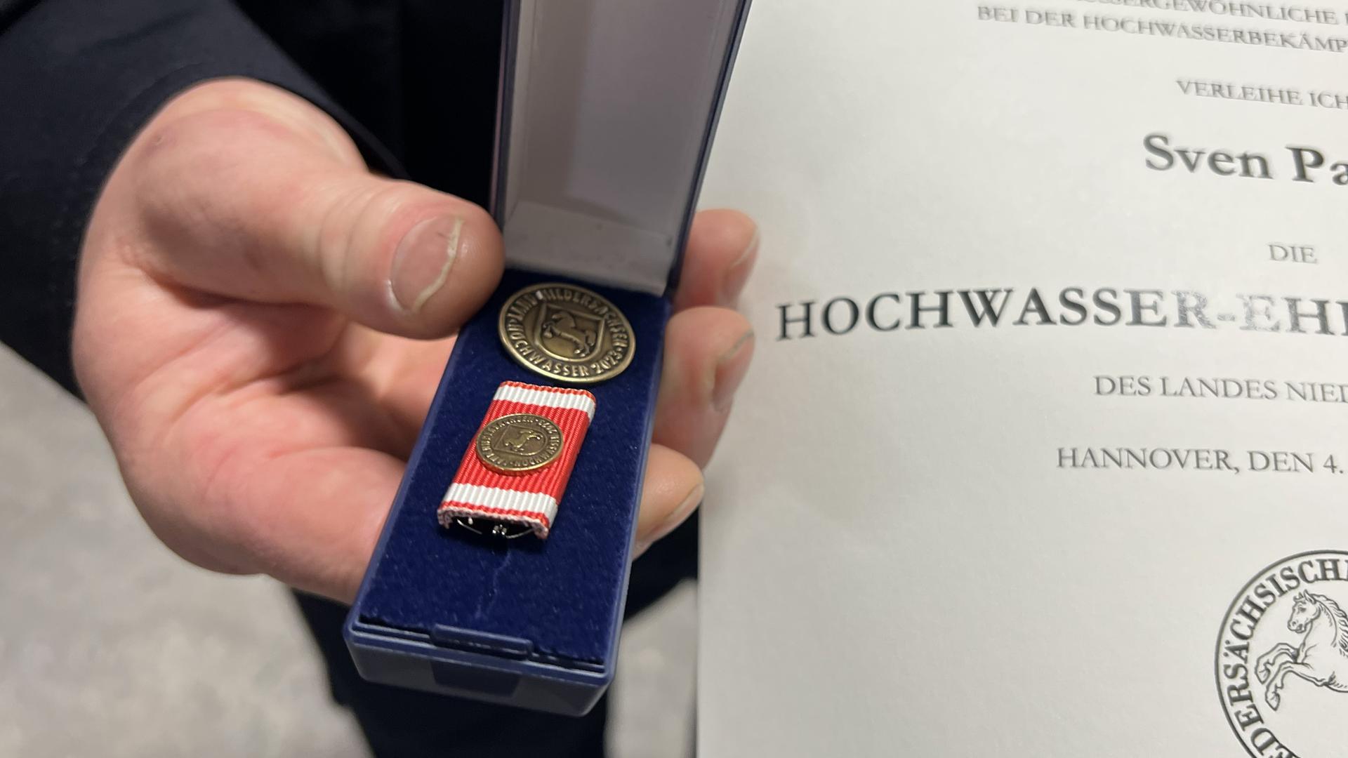 Ein Feuerwehrmann hält eine Ehrennadel in der Hand. | NDR, Jan Fragel