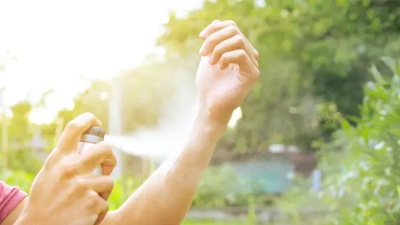 Eine Person sprüht sich ein Mückenschutzspray auf den Arm