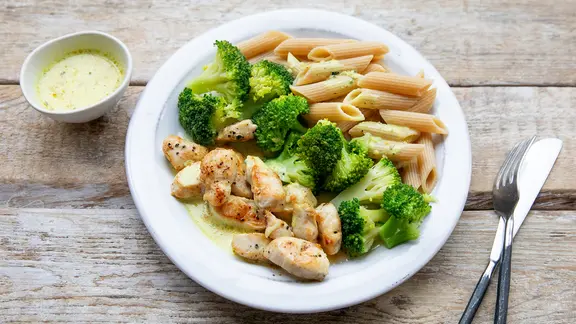 Auf einem Teller liegt ein Gericht mit Hähnchenfleisch, Pasta und Brokkoli.