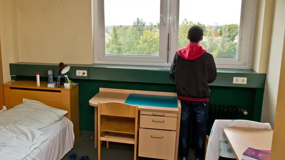 Ein Junge steht in einem Zimmer und schaut aus dem Fenster.
