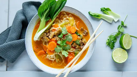 Eine Schale mit Curry-Ramen-Suppe, am Schalenrand ein Blatt Pak Choi sowie ein paar Stäbchen.