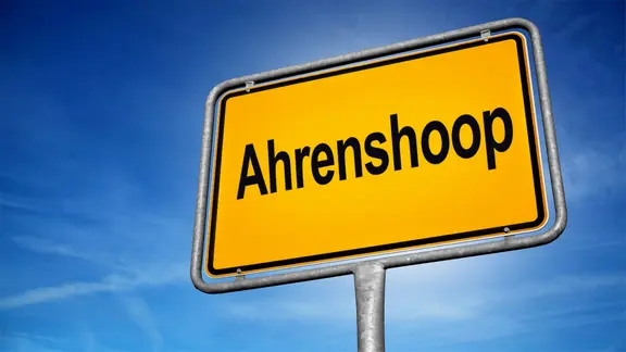 Ein Ortsschild vor blauem Himmel mit der Aufschrift Ahrenshoop. (Montage)