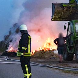 Brand in Hagermarsch: Mehrere Feuerwehrleute stehen vor dem Feuer. Ein Trecker hilft der Feuerwehr.