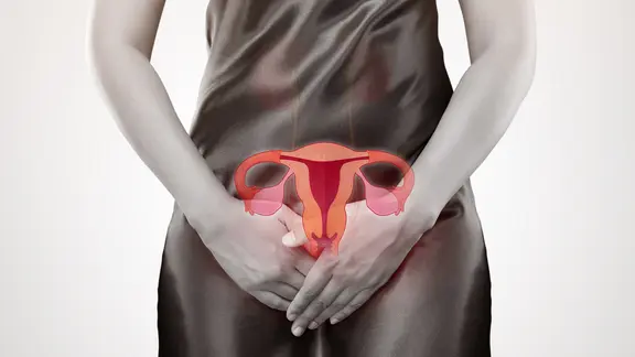 Gebärmutterhalskrebs, Symbolbild: Frau im Kleid hält sich die Hände vor dem Unterleib. Darüber ist eine Grafik, die die Gebärmutter und Eierstöcke zeigt.