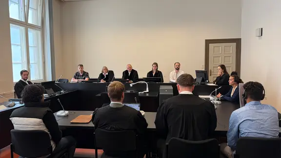 Mehrere Personen sitzen in einem Gerichtssaal. 
