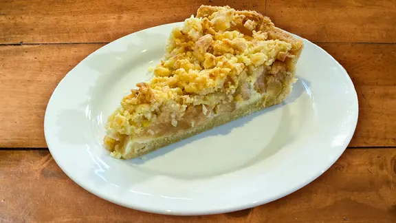 Apfelkuchen mit Sahneguss auf einem Teller angerichtet
