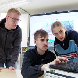Drei Jugendliche sitzen an einem Laptop in einem Klassenzimmer.