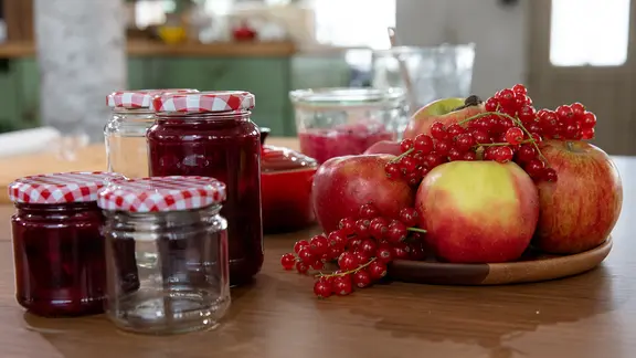 Beeren-Apfelmarmelade in Gläsern und frische Früchte auf einer Arbeitsplatte.