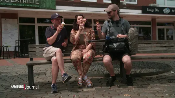 Zwei Mänenr und eine Frau sitzen auf der Bank und essen Eis.