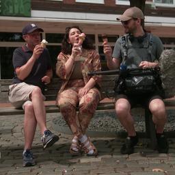 Zwei Mänenr und eine Frau sitzen auf der Bank und essen Eis.