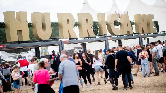 Zahlreiche Festivalbesucher gehen am Eingang des Hurricane Festivals unter dem Schriftzug "Hurricane" hindurch.