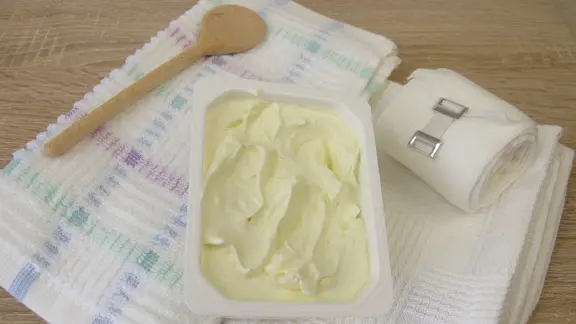 Ein Kochlöffel, Quark, Tücher und ein Verband liegen auf einem Tisch.