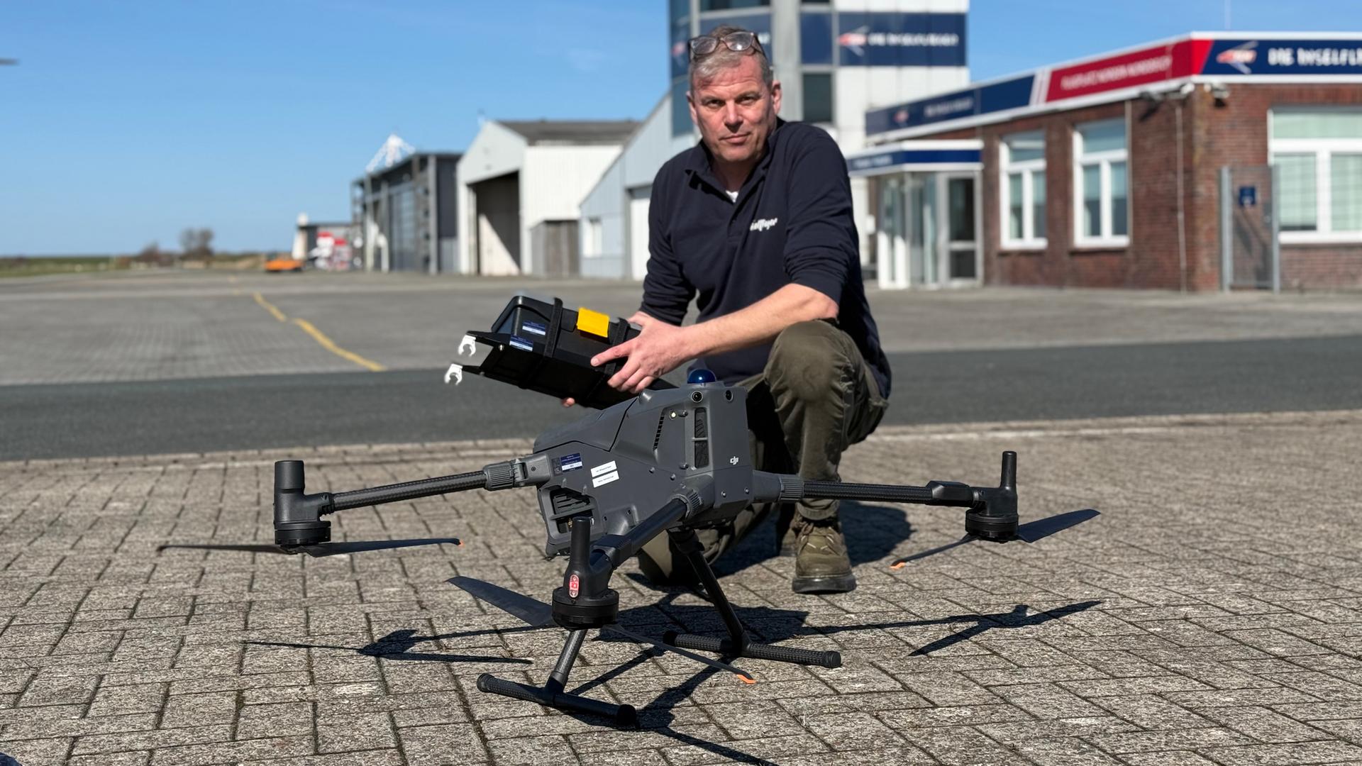 Eine Drohne am Flugplatz Norden-Norddeich, dahinter kniet ihr Pilot Ingo Hellmann. | NDR, Thees Jagels