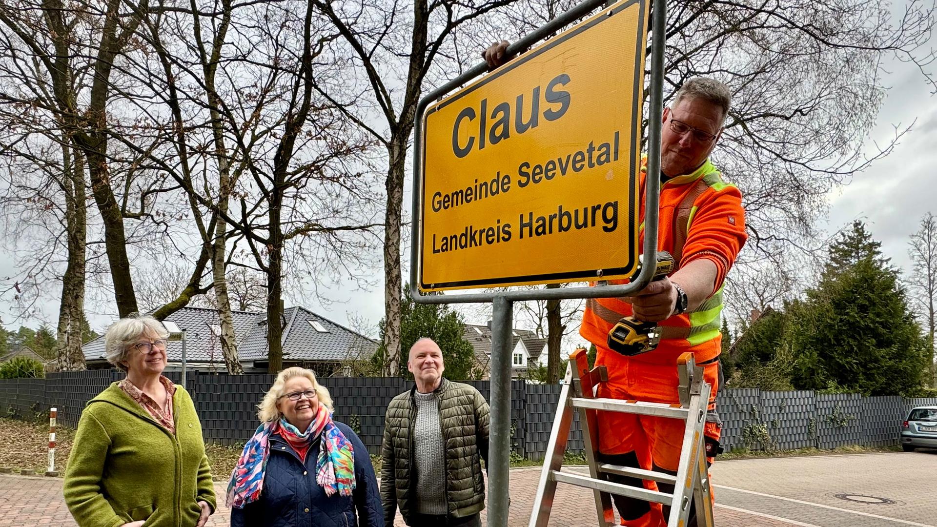 Mehrere Personen sind dabei, als das Ortsschild 