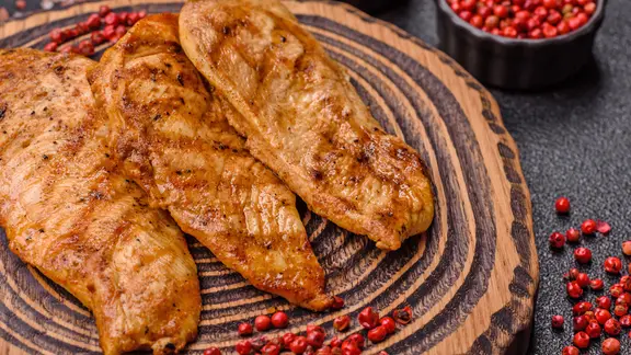 Drei Stücke gegrilltes Huhn auf einem Teller, daneben rote Pfefferkörner.