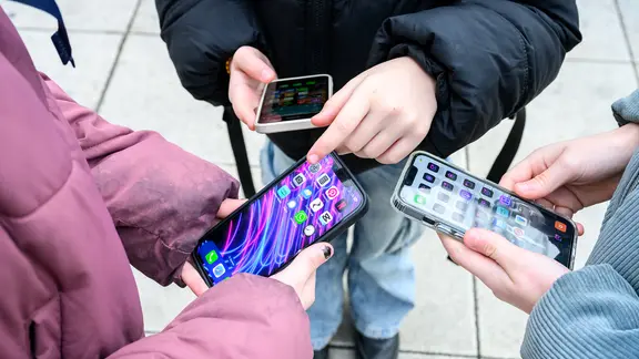 Drei Schüler*innen stehen mit Handys auf dem Pausenhof.