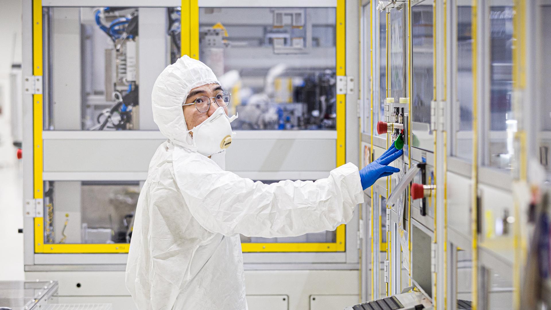 Ein Mitarbeiter arbeitet mit weißem Schutzanzug in einem Reinraum einer Batteriefabrik | picture alliance/dpa | Moritz Frankenberg