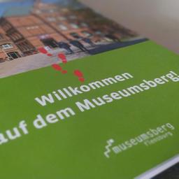 Ein Heft mit dem Schriftzug "Willkommen auf dem Museumsberg!" liegt auf einem Tisch