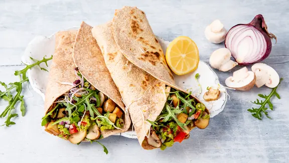 Zwei mit Gemüse gefüllte Vollkornwraps auf einer Porzellanplatte.