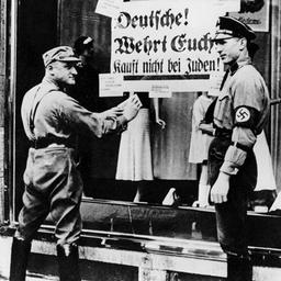 SA-Männer kleben ein Plakat mit der Aufschrift 'Deutsche! Wehrt Euch! Kauft nicht bei Juden' an die Schaufensterscheibe eines jüdischen Geschäfts.