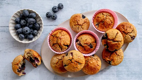 Ein Teller mit Buttermilch-Muffins, daneben eine Schale Blaubeeren.