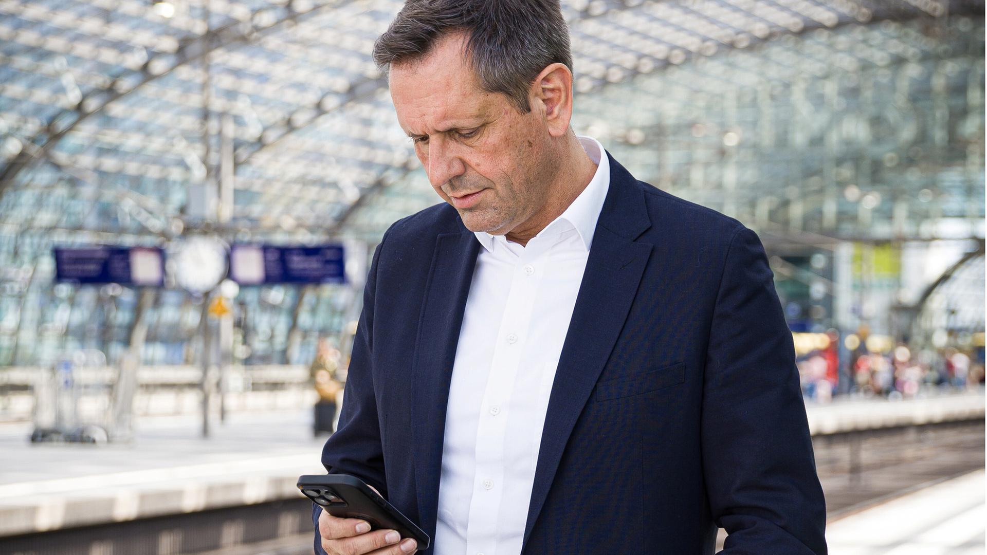 Ministerpräsident Olaf Lies steht auf einem Bahnsteig und schaut auf sein Mobiltelefon. | picture alliance/dpa, Moritz Frankenberg