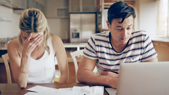 Eine Frau und ein Mann sitzen sorgenvoll vor einem Laptop.
