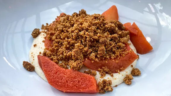 Pochierte Quitten mit Grießbrei und Haselnuss-Streuseln auf einem Teller serviert