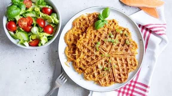 Ein Teller mit Süßkartoffel-Waffeln, daneben steht eine Schüssel mit Salat