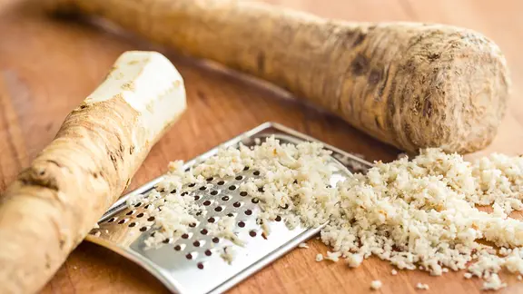 Frischer Meerrettich liegt neben einer Küchenreibe