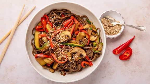 Eine Schale mit Nudeln, darauf Champignons und anderes Gemüse sowie Sesamkörner.