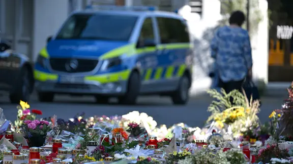 Blumen und Kerzen sind in Solingen zu sehen, dahinter ein Polizeiwagen. Bei einem Stadtfest waren dort drei Menschen mit einem Messer getötet worden.