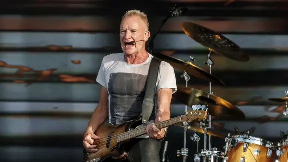 Der Musiker Sting spielt Bass auf einer Bühne und singt.