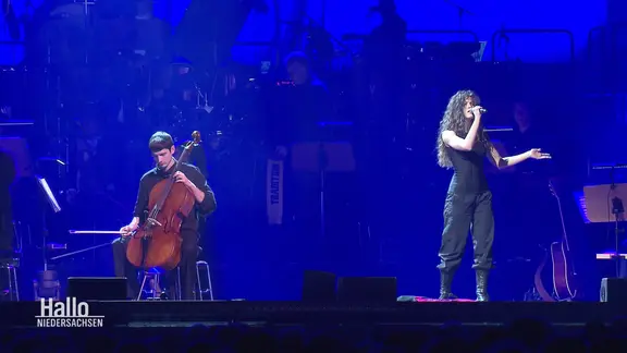 Das ESC-Duo Abor & Tynna tritt auf einer Bühne auf. Er am Cello, sie singt in ein Handmikrofon.