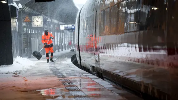 Winterdienst-Mitarbeiter schieben Schnee von einem Bahnsteig am Hamburger Hauptbahnhof. | dpa Bildfunk, Christian Charisius/dpa Winterdienst-Mitarbeiter schieben Schnee von einem Bahnsteig am Hamburger Hauptbahnhof.