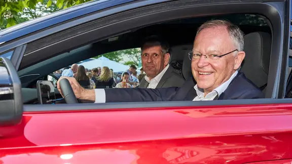 Stephan Weil sitzt am Steuer eines roten Autos, auf dem Beifahrersitz sitzt Olaf Lies.