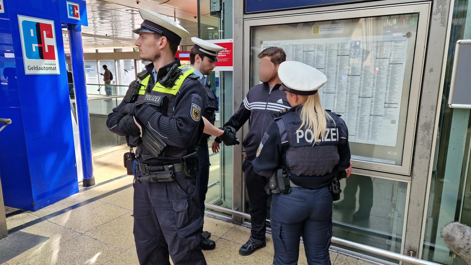 Drei Polizeibeamte stehen im Kreis um einen Mann bei einer Polizeikontrolle im Hauptbahnhof Hannover. | NDR, Maren Bruns