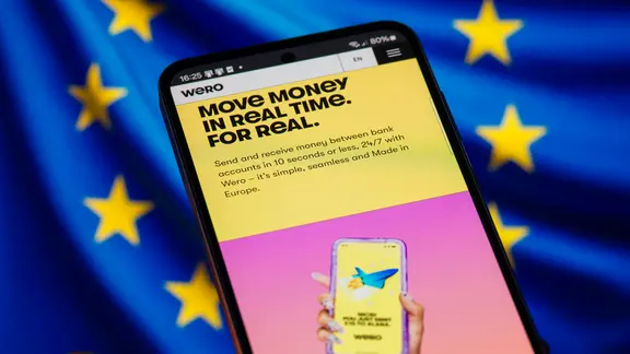 Handydisplay mit Bezahldienst Wero, im Hintergrund eine EU-Flagge.
