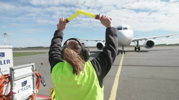 Eine Fluglotsin steht vor einem Flugzeug und gibt ein Signal.